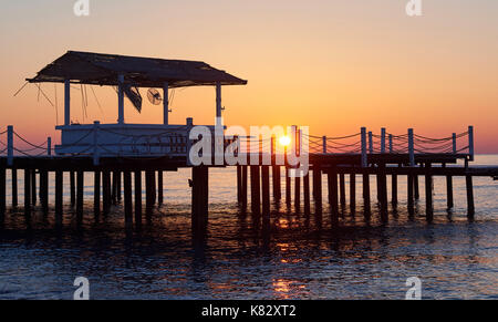 gazebo on the wooden pier into the sea with the sun at sunset Stock Photo