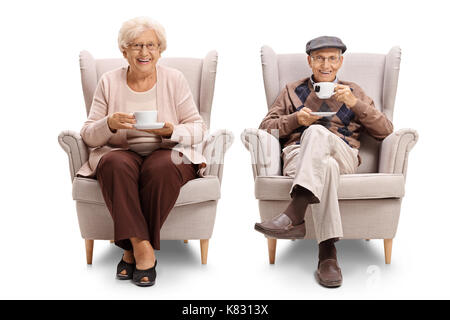 Seniors seated in armchairs drinking tea and looking at the camera isolated on white background Stock Photo
