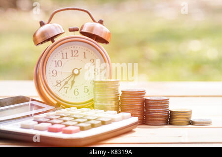 save money for future, pile of coins on wood table with calculator and alarm clock on green garden background Stock Photo