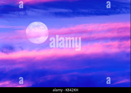 Moon clouds is a colorful surreal fantasy like pink and blue cloudscape with a magical surreal full moon rising in the night sky. Stock Photo