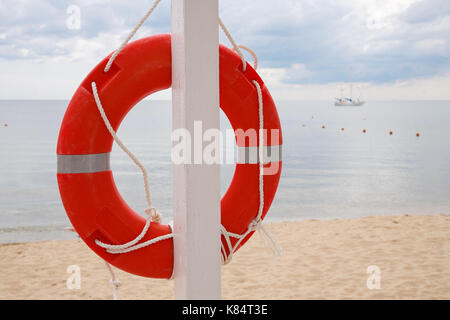 Life ring hanging on a pillar, on the beach against the sea Stock Photo