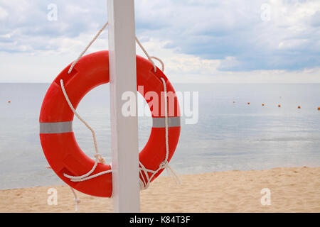 Life ring hanging on a pillar, on the beach against the sea Stock Photo