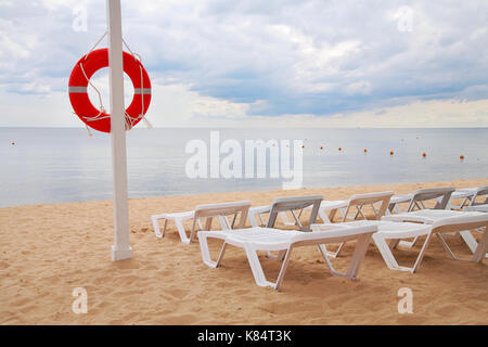 Life ring hanging on a pillar and sun beds on the beach against the sea Stock Photo