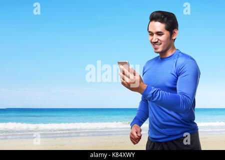 Young asian man using mobile phone before going for a run on the beach Stock Photo