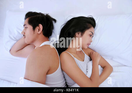 Upset asian couple having problems with lying side by side in bed facing in opposite directions in bed