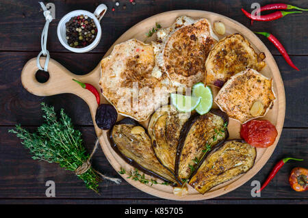 Baked vegetables: eggplant, patisson, tomatoes on a round wooden stand on a dark background. Top view. Vegan dish.