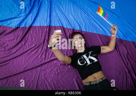 A woman is seen taking a selfie while holding a small LGBT flag in her hand during the yearly Belgrade Gay Pride. Gay Pride in Serbia has been held since 2001, and this event is the fourth in a row that goes without problems as a large recent Serbian politicians including the prime minister Ana Brnabi? and mayor of Belgrade Siniša Mali. started to support the Gay parade and the LGBT community. On September 17, 2017 in Belgrade, Serbia. Stock Photo