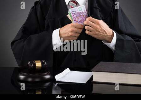 Close-up Of Male Judge Hiding Banknote At Desk Stock Photo