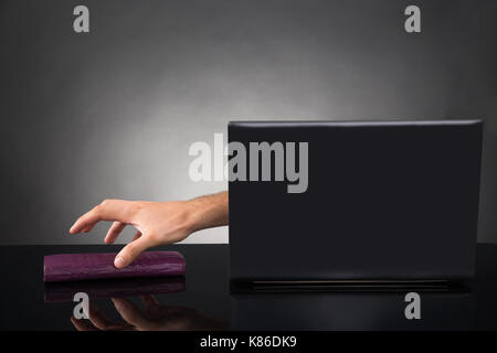 Close-up Of Person Hands Reaching Out From A Laptop Grabbing Wallet At Desk Stock Photo
