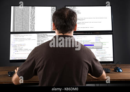 Young Man Programming Code On Computers Screen At Desk Stock Photo