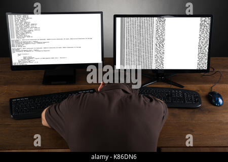 Man Sleeping At Desk With Computers Showing Program Code Stock Photo