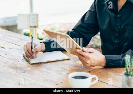Business man hand holding tablet and writing notebook in coffee shop. Stock Photo