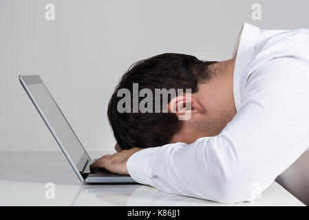 Side view of stressed businessman leaning on laptop at desk against white background Stock Photo