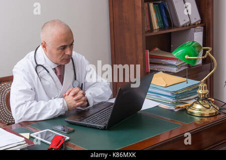 Aback doctor in his studio. Use new technologies. The office has an antique desk and a green lamp shade of green. Stock Photo