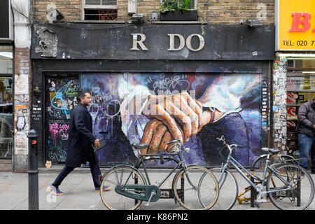 A man walks past an empty shop covered in graffiti, Brick Lane, London. Stock Photo