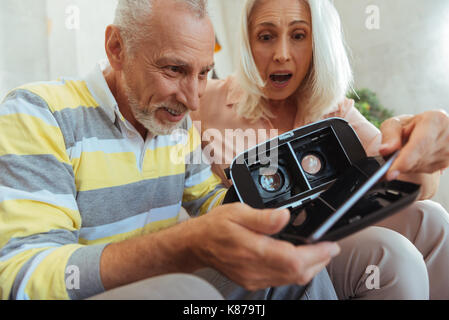 Positive surprised aged couple trying up VR glasses Stock Photo