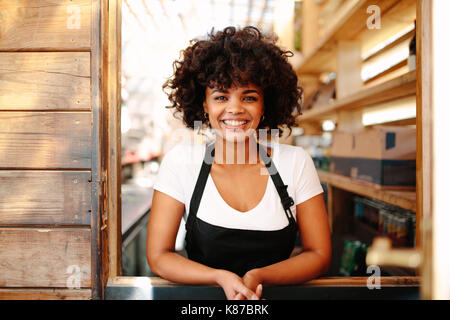 Woman barista inside her coffee shop. Curly haired woman  bartender in cheerful mood standing behind the counter. Stock Photo