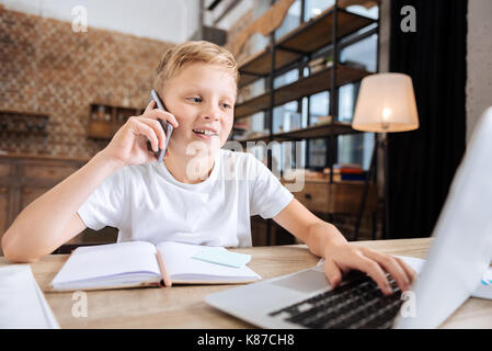 Pre-teen boy talking on the phone while using laptop Stock Photo