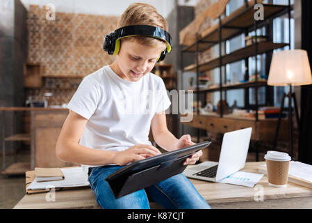 Pleasant boy wearing headphones and playing on tablet Stock Photo