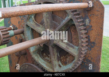 Close up of old rusted and worn machinery re industrial heritage cogs and wheels on grassy surface located near Nigg Scotland Cromarty Firth Stock Photo