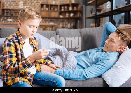 Caring son checking temperature of his ill father Stock Photo
