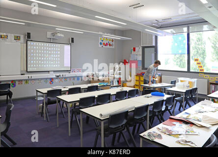 A teacher works alone in a modern classroom in a new London secondary school. Traditional layout with desks facing a large monitor screen. Stock Photo