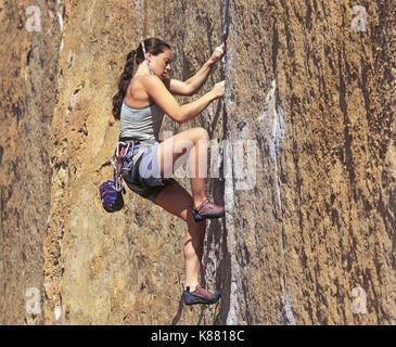 A young, female rock climber scales a vertical cliff at Smith Rock State Park in central Oregon near the town of Terrebonne. Smith Rock is one of the  Stock Photo