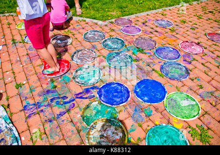 children playing making colorful designs with their feet immersed in the colorful tempera Stock Photo