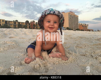 A cute, smiling, baby has a fun in the warm sand. This is his first time experiencing sand. Stock Photo