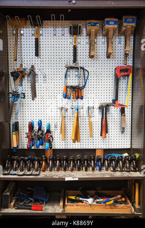 Work bench in a boat-builder's workshop, selection of hand tools for wood working hanging on a wall. Stock Photo