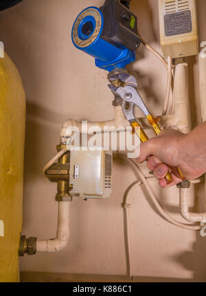 A plumber working in an airing cupboard, using an adjustable wrench to work on a defective central heating pump. England, UK. Stock Photo