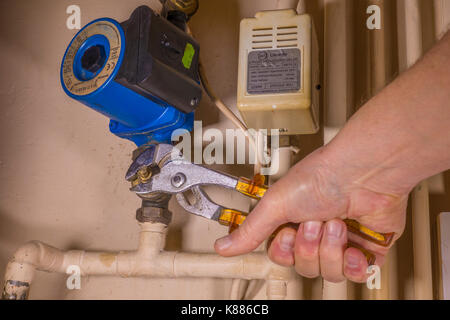 A plumber working in an airing cupboard, using an adjustable wrench to work on a defective central heating pump. England, UK. Stock Photo