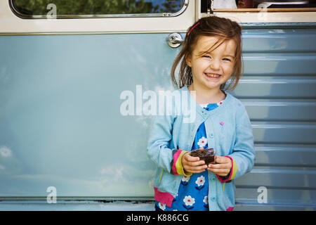 Smiling girl standing in front of blue mobile coffee shop, holding chocolate brownie. Stock Photo