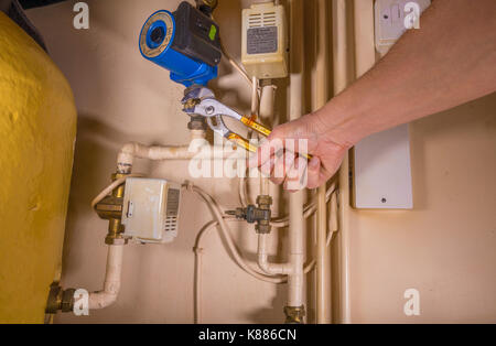 A plumber working in an airing cupboard, using an adjustable wrench to work on a defective central heating pump. England, UK. Stock Photo