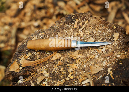 A carving knife with wooden handle lying on splitting block covered in wood shavings. Stock Photo