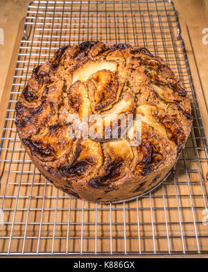 A whole spiced apple cake, cooling on a rack, on a wooden surface, in a kitchen, freshly baked from the oven. England, UK. Stock Photo