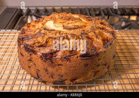 A whole spiced apple cake, cooling on a rack, on a wooden surface, in a kitchen, freshly baked from the oven. England, UK. Stock Photo