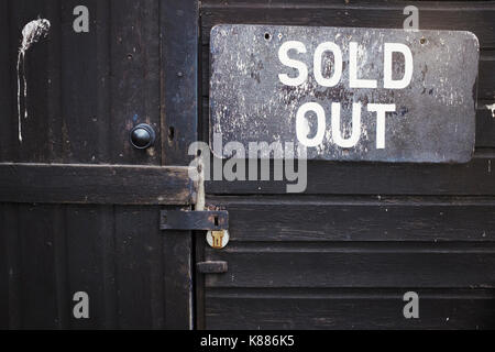 Close up of 'Sold Out' sign on black wooden wall beside a closed door. Stock Photo