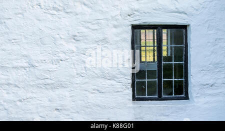 white, stone wall with a black window frame inset into the stone of an old Welsh Chapel Stock Photo