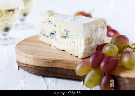 Blue cheese  served with fresh grapes and two glasses of white wine on rustic cutting board, cheese platter Stock Photo