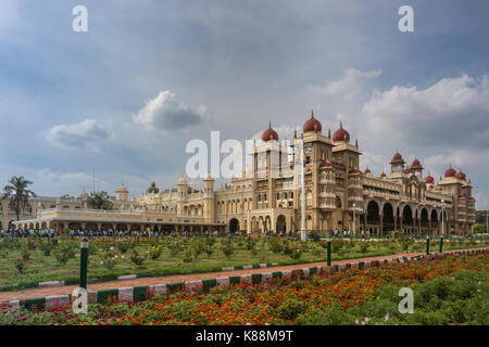 Mysore, India - October 27, 2013: Wide shot out of garden of South and East facades of Mysore Palace under cloudscape. Yellow building with towers and Stock Photo