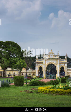 Mysore, India - October 27, 2013: Green garden with flowers in front of closed North Gate to Mysore Palace under cloudscape. Stock Photo