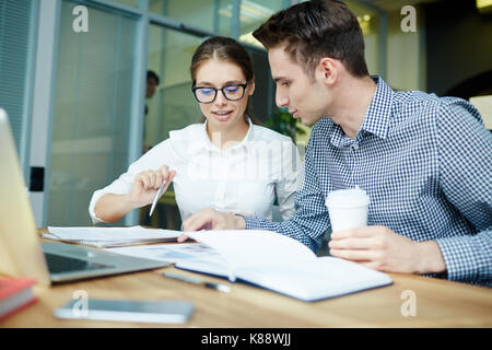 Young financial managers analyzing statistics while having working meeting at spacious open plan office, handsome man holding paper cup of coffee in h Stock Photo