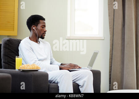 Young man with earphones listening to music and networking at home Stock Photo