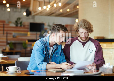 Group of talented financial managers analyzing results of accomplished work while having working meeting at cozy small coffeehouse, blurred background Stock Photo