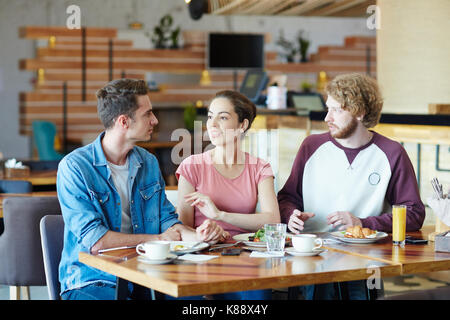 Multi-ethnic group of friends enjoying delicious lunch at cozy small cafe while having long-awaited gathering, lovely interior on background Stock Photo