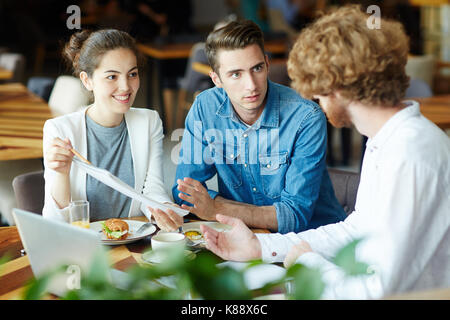 Multi-ethnic group of talented interior designers presenting ideas concerning joint project to their bearded client while having meeting at cozy resta Stock Photo