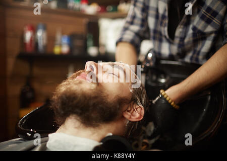 Young client of haircare salon having his hair washed with shampoo by master Stock Photo