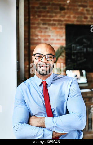 Elegant and cheerful businessman in blue shirt and red tie leaning against wall of office Stock Photo