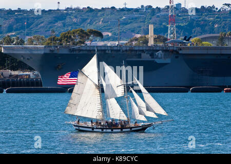 Tall Sailing Ship Anazing Grace under full sail on San Diego Bay, CA US with aircraft carrier in background  Amazing Grace is a 83' topsail schooner b Stock Photo